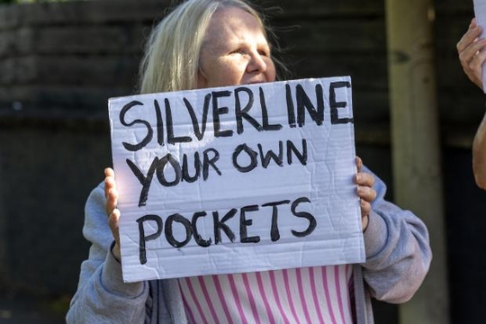 A striking Silverline care worker holds a placard that reads "Silverline your own pockets"
