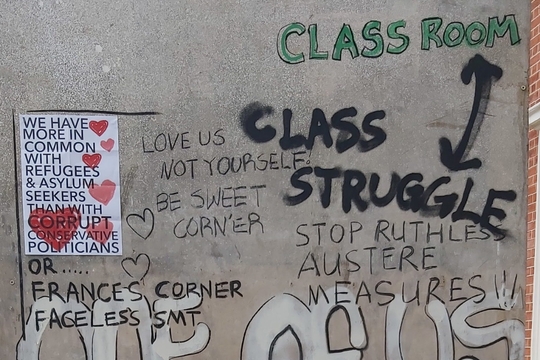 Graffiti-covered wall with phrases like "Class Struggle - Class Room," "Stop Ruthless Austere Measures," and "We have more in common with refugees."